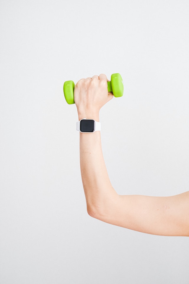 Person wearing white apple watch while holding a green dumbbell.