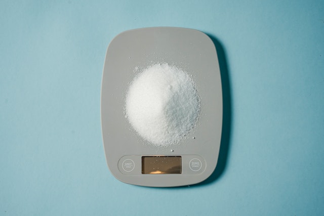 An electronic food scale with sugar on top.