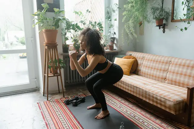 Curly-haired woman in sports attire doing squats in a living room.