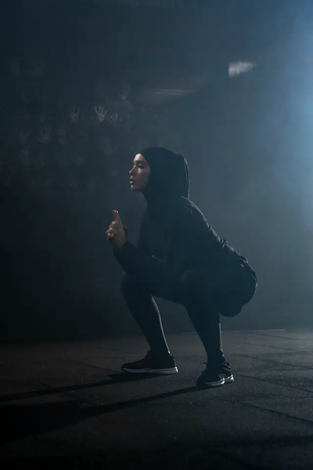 A woman in black sportswear squatting.