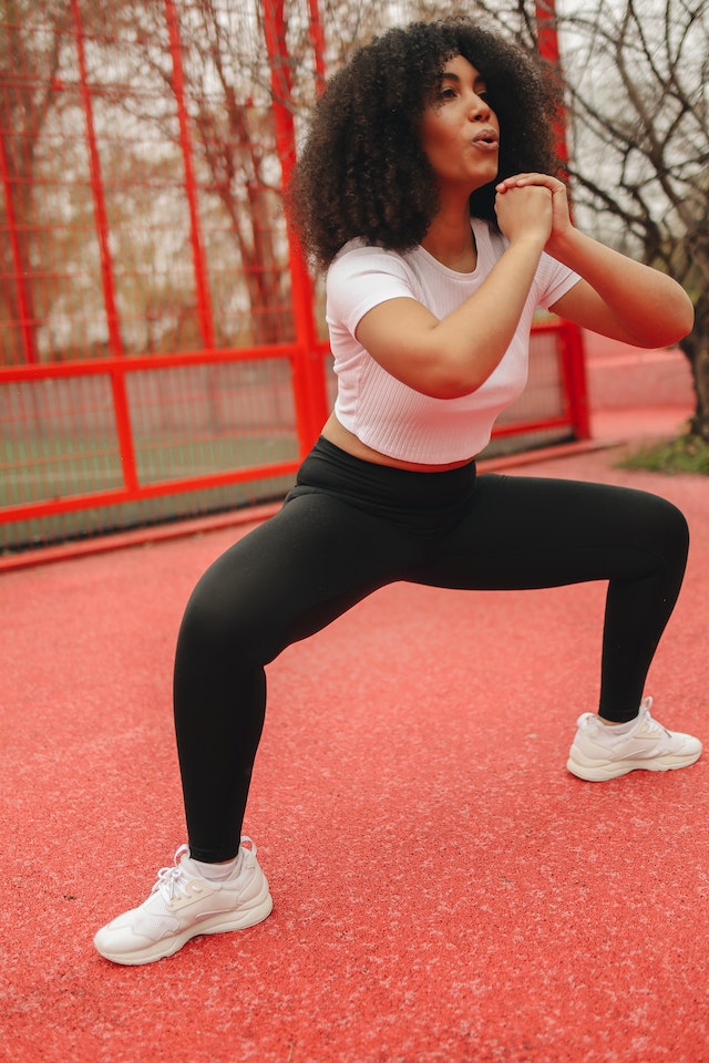 A woman performing sumo squats wearing a black and white workout outfit. 