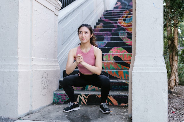 A woman squatting at the bottom of a set of stairs. 