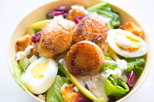 A healthy bowl of fresh vegetable salad, topped with sliced boiled eggs.
