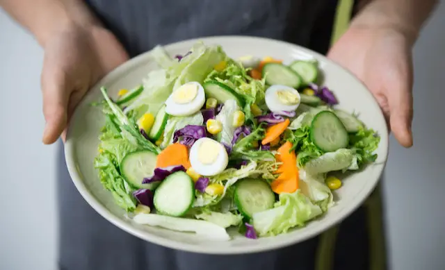 A bowl of delicious green salad topped with sliced chicken eggs, cucumber, and red cabbage