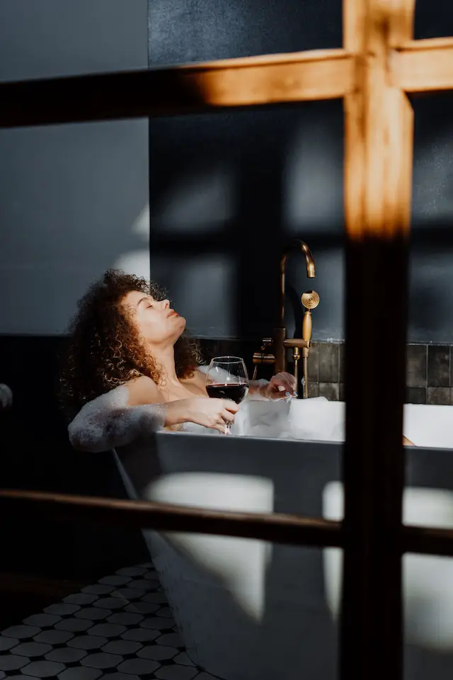 A woman relaxing in a nice bubble bath while holding a glass of wine.
