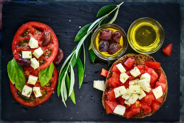 A bowl of tomato salad on bread, with two shots of olive oil on the side.