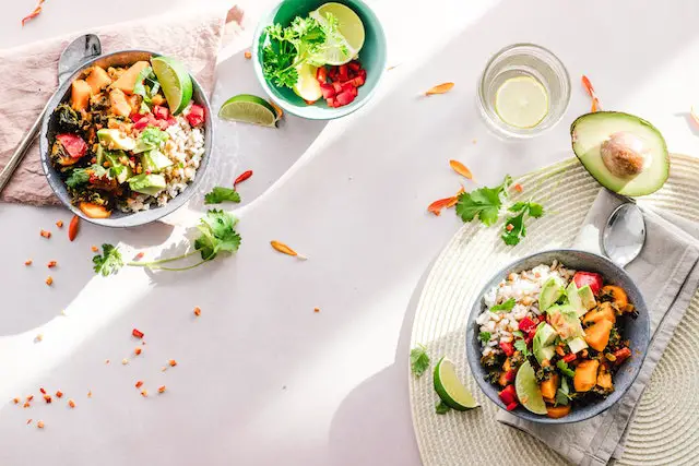 Two bowls of nicely plated vegetable salads with a slice of lime and avocado on the side.