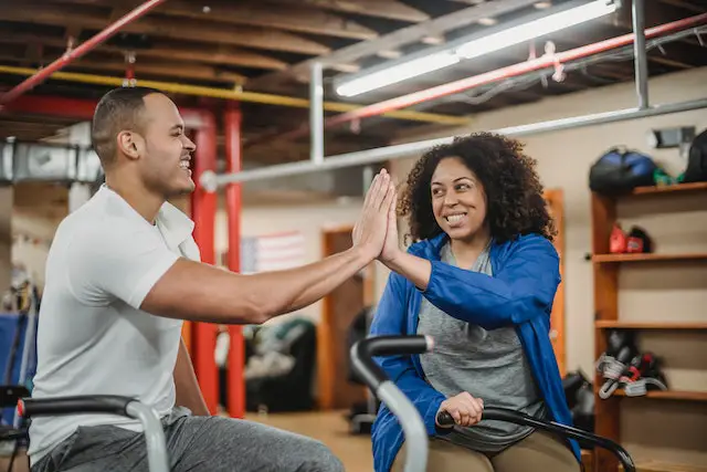 Male gym instructor and curly haired woman doing a high-five at the gym.