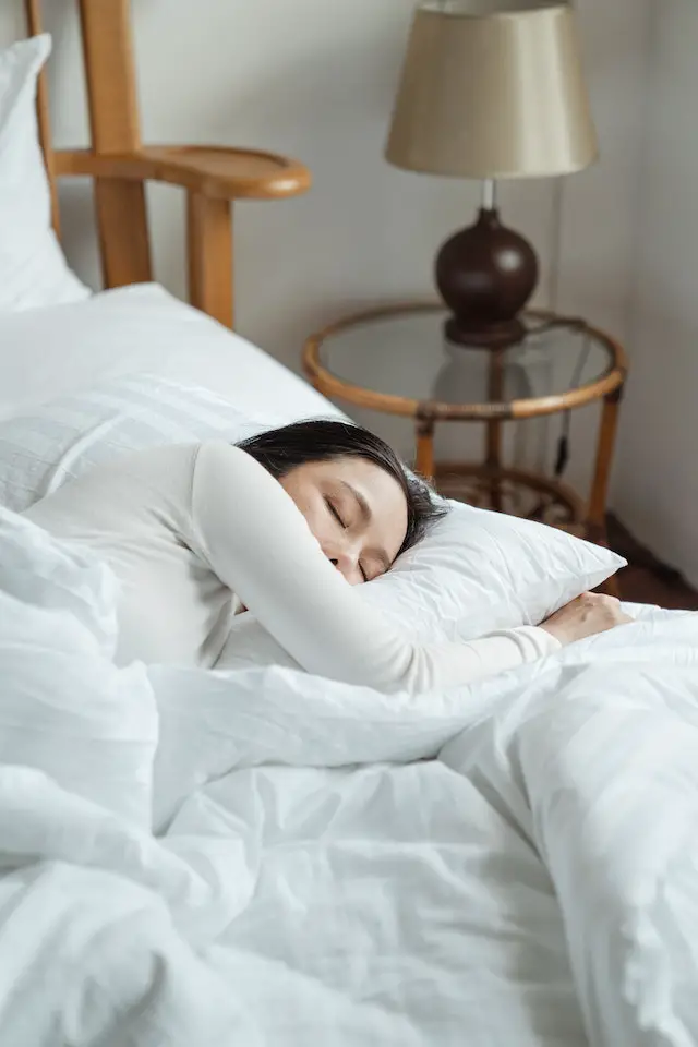 A young woman sleeping soundly in a bed of white sheets and pillow.