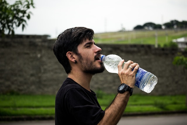 A man in black shirt drinking from a water bottle.