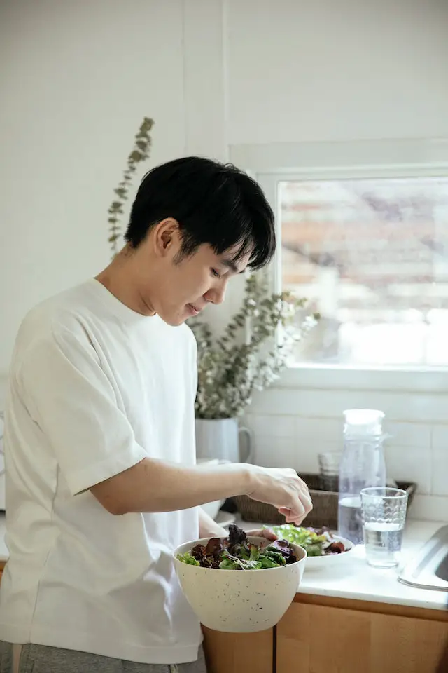 Black-haired man preparing a bowl of fresh leafy salad.
