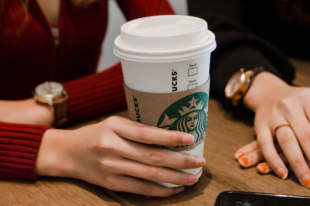 A woman holding a white Starbucks coffee cup with a sleeve.
