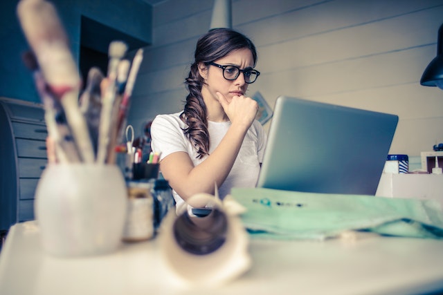 A woman wearing a pair of glasses and doing research on her laptop.