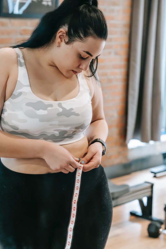 A woman measuring her waist with a tape measure.