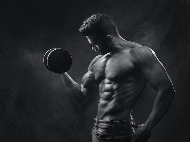 A muscular man holding a black dumbbell.