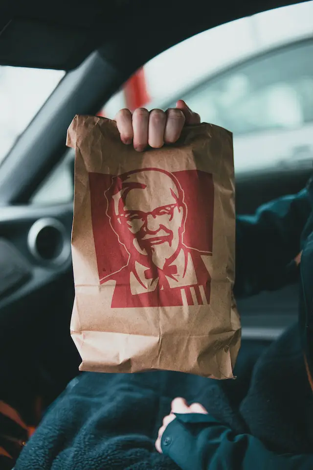 A close-up shot of a person holding a brown paper bag from KFC.