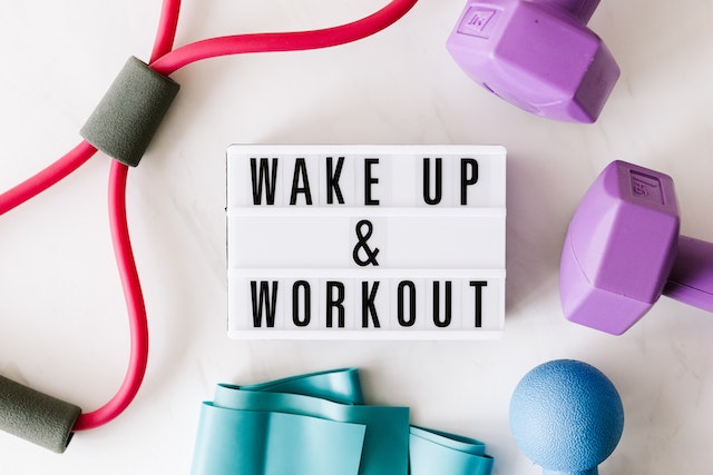 A "Wake up and workout sign" on a white light box surrounded by dumbbells and exercise mat.