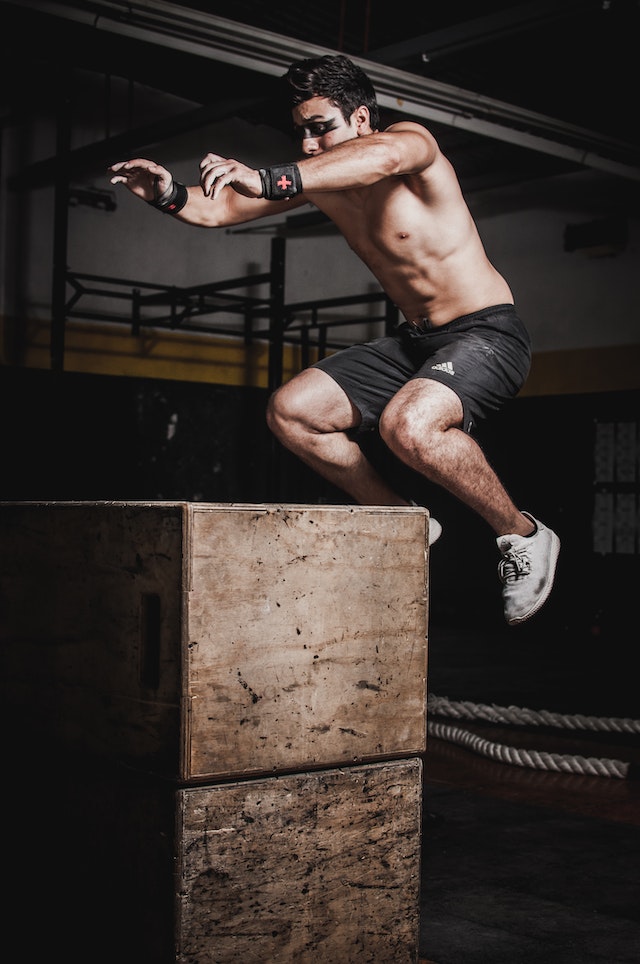 A shirtless man training and jumping on a gym box.