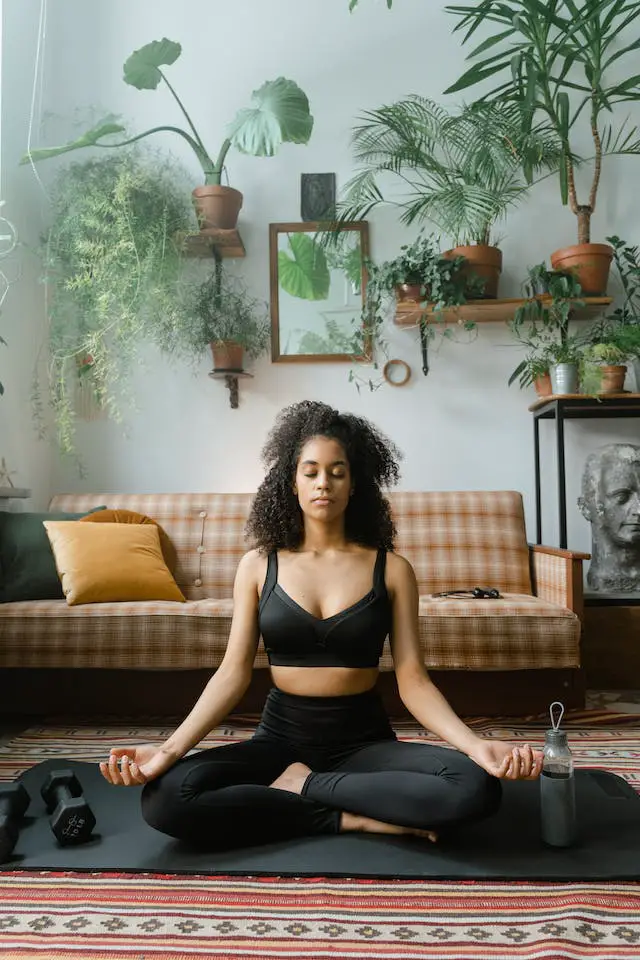 A curly-haired woman in black sports attire meditating before working out.