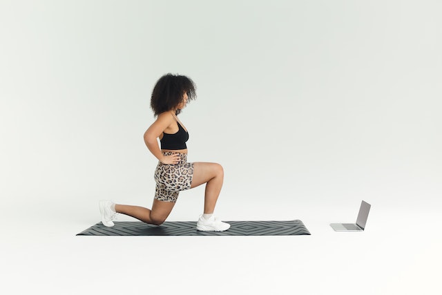 A woman doing knee lunges while watching an online workout video on her laptop.
