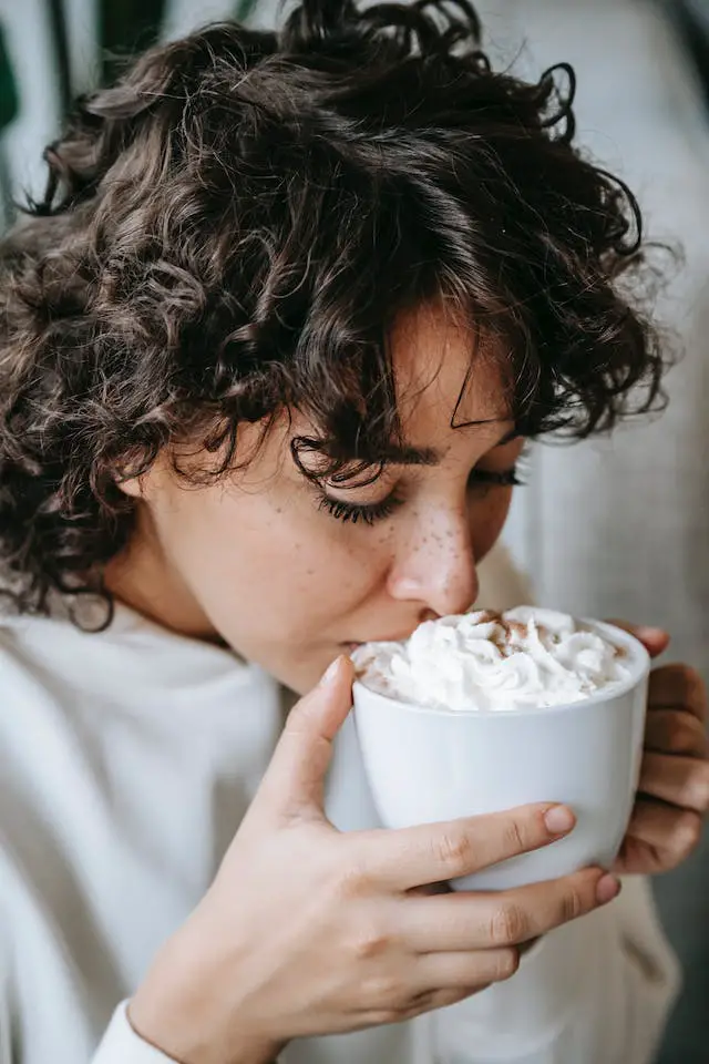 A woman drinking a cup of hot coffee with whipped cream.