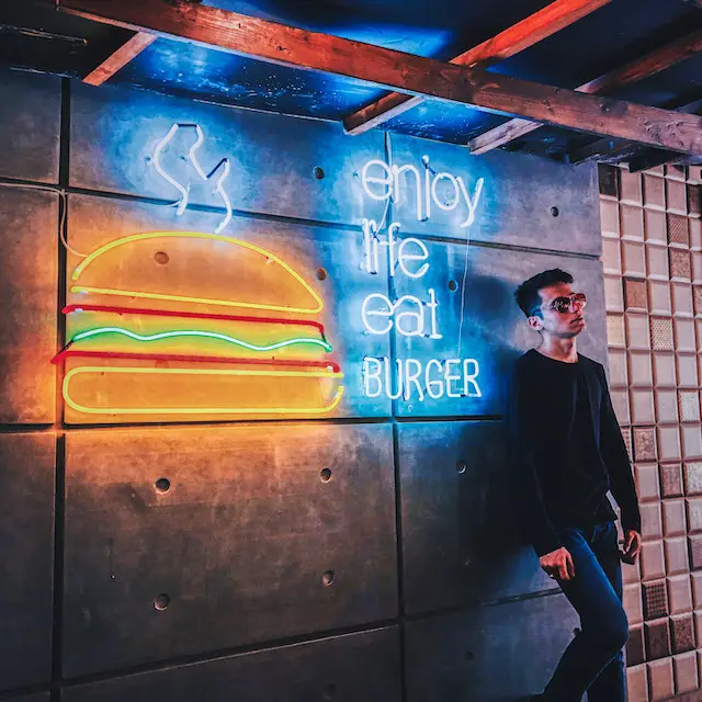 A man leaning on a wall with an "Enjoy life, eat burger" signage.