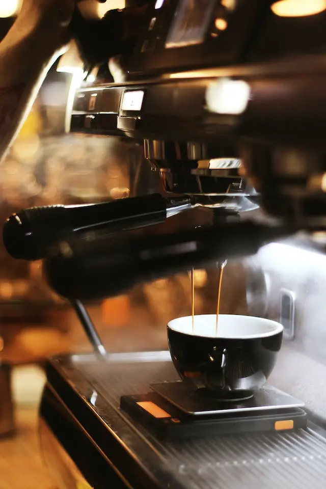 A black brewing machine extracting a cup of espresso.
