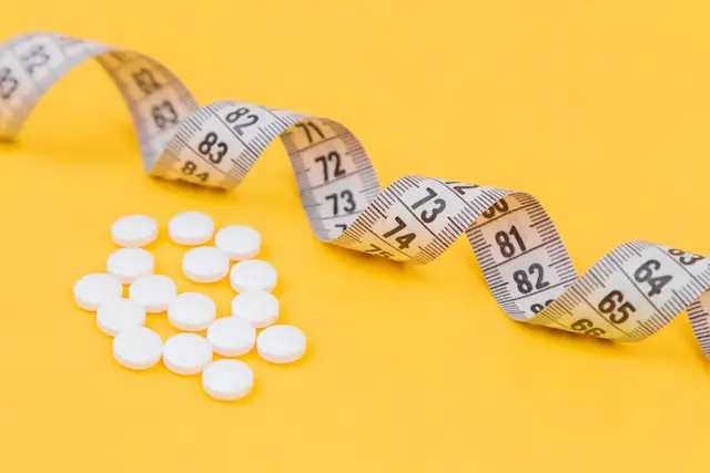 White medication pills and a measuring tape on a yellow surface
