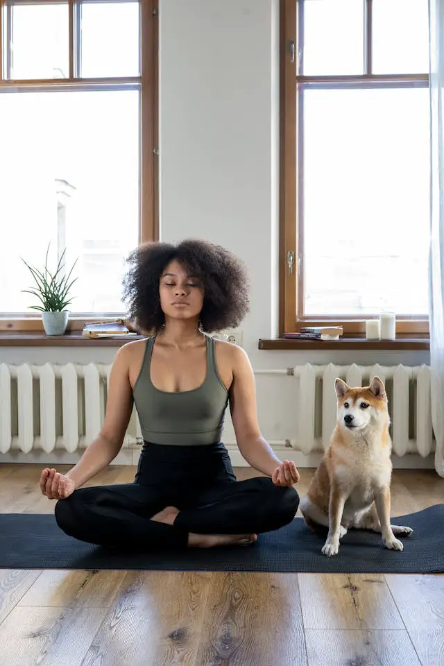 Woman sitting cross-legged, meditating next to her dog on a yoga mat.