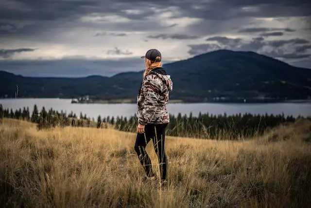 A woman in hiking attire standing on a grassy hill overlooking a lake.