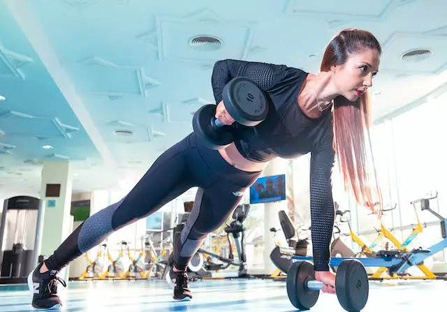 A long-haired woman in sports attire doing renegade rows in the gym