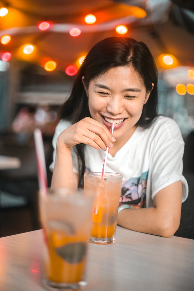 A woman sipping her orange-infused iced drink at a cafe.