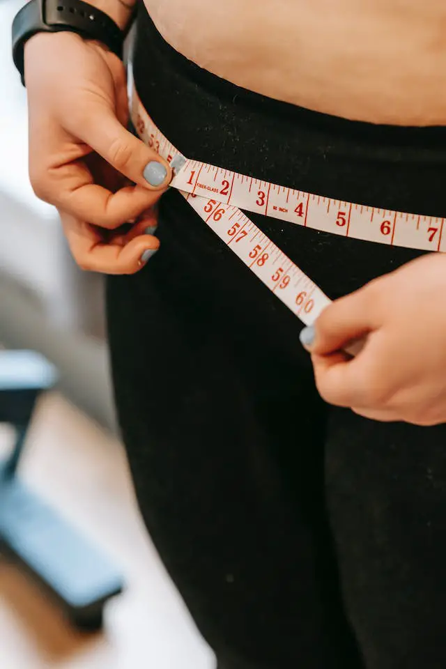 A woman measuring her waist using a tape measure