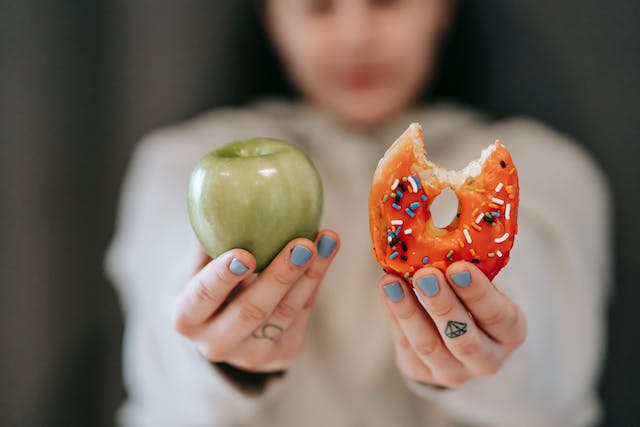 A woman showing a bitten apple and a bitten donut.