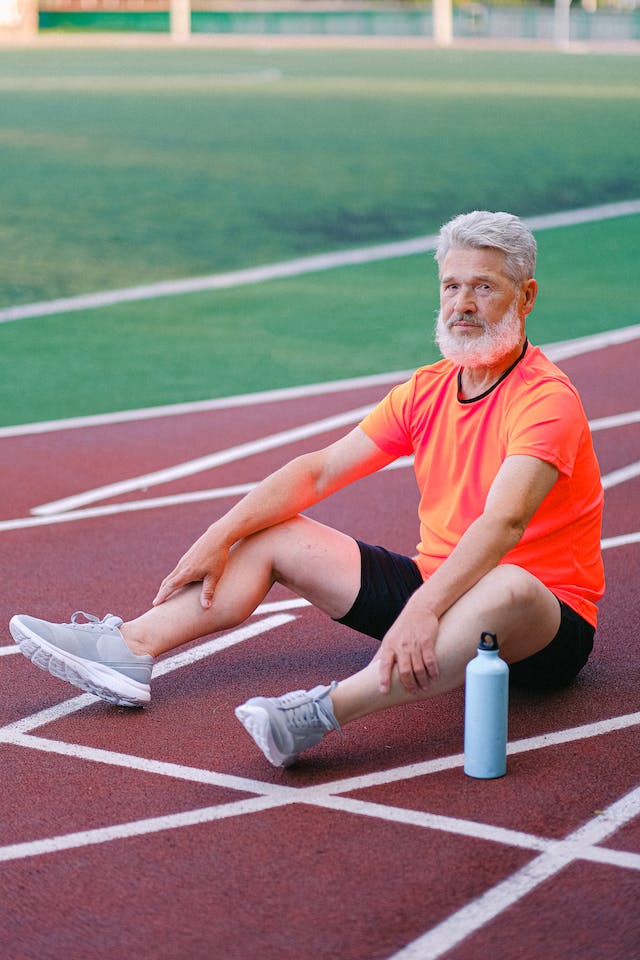 A man in an orange shirt on a seated resting position at the running track.