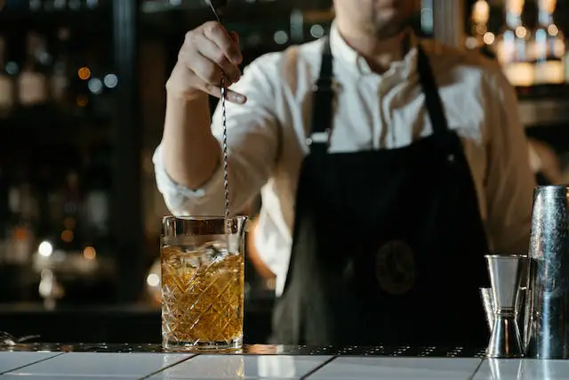 A bar man stirring a cocktail drink using a bar spoon.