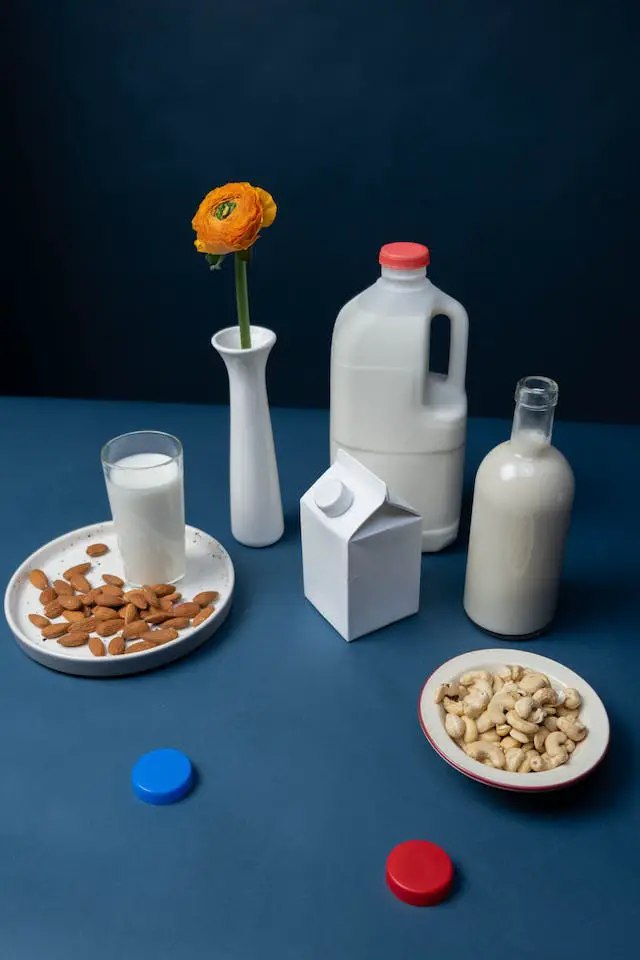 Two fresh milk container and a glass of milk beside two small plates of almond and cashews
