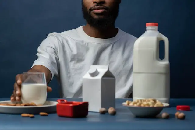 Two fresh milk container and a glass of milk beside two small plates of almond and cashews
