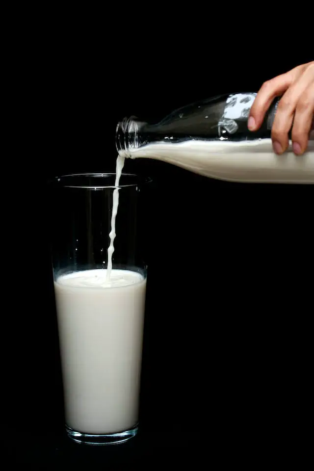 A person pouring milk in a highball glass.