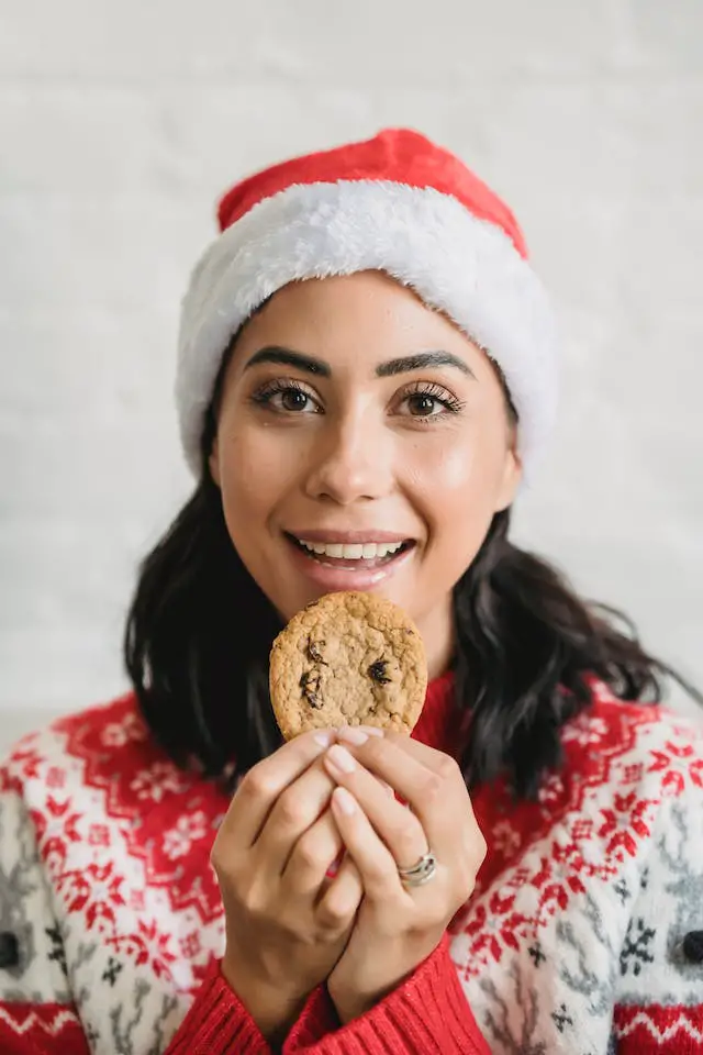 A woman in Christmas costume holding up a cookie with her two hands.