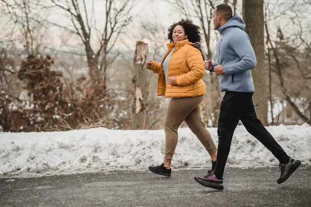 A couple running together in a snowy park.