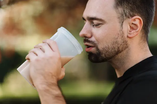 A man in a black shirt holding a tumbler of protein shake.