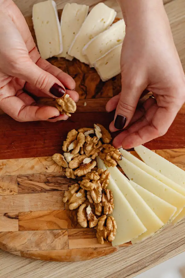 A woman arranging walnuts and cheese on a wooden board.