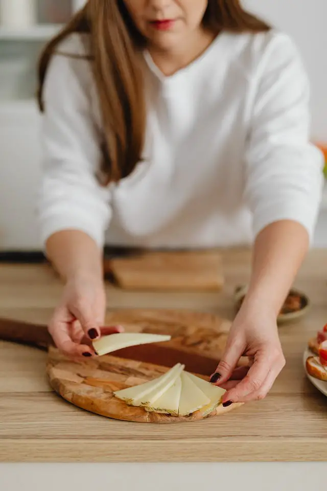 A woman in white top arranging slices of cheese on a wooden chopping board.