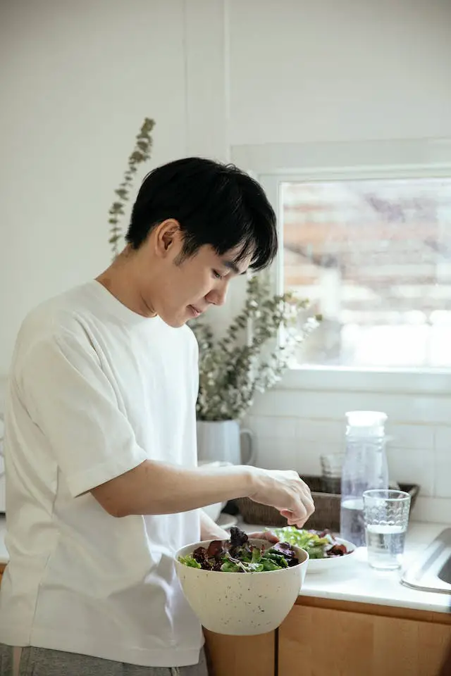 his kitcAn man holding a bowl of leafy salad in his kitchen.