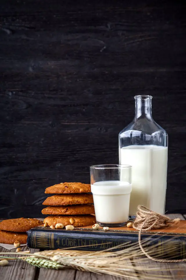 A stack of cookies, a glass and a bottle of milk placed on top of hard-bound book.