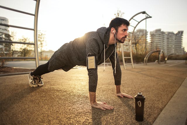 A man in gray jacket doing pushups during sunrise.