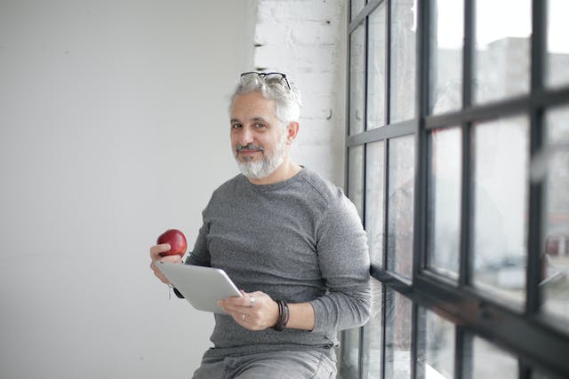 A smiling man holding an apple and an iPad.