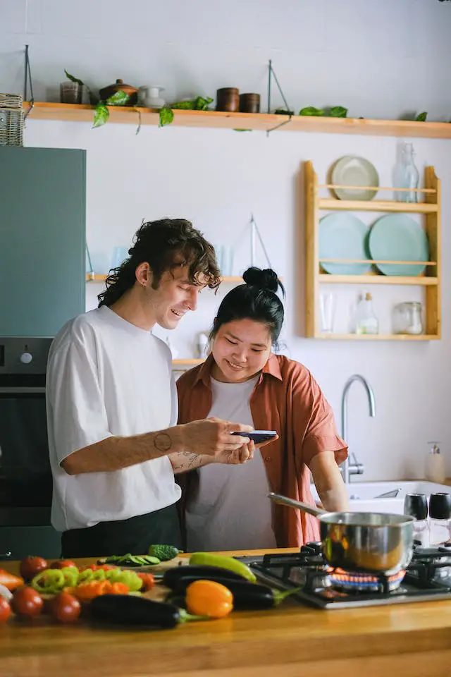 A man and a woman looking at a smart phone in the kitchen.