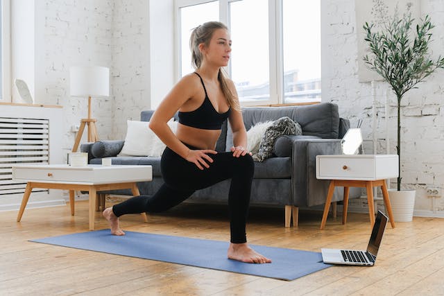A woman on a yoga mat following an online exercise from her laptop.